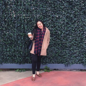 Woman in winter clothing posing in front of a green wall at the Dallas Farmers Market