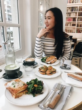 Woman looking out of a window in a Parisian inspired cafe with French food and coffee in front of her