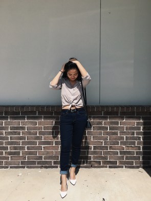 Woman posing in a taupe button up, jeans, and white heels