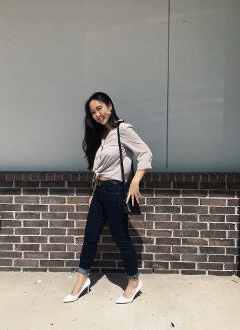 woman posing wearing jeans with a black belt and a taupe button up top with white Jessica Simpson heels